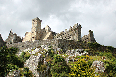 Senior Class Trips 4 Stone castle ruins atop a rocky hill, surrounded by greenery. The sky is cloudy, casting soft light on the ancient structures.
